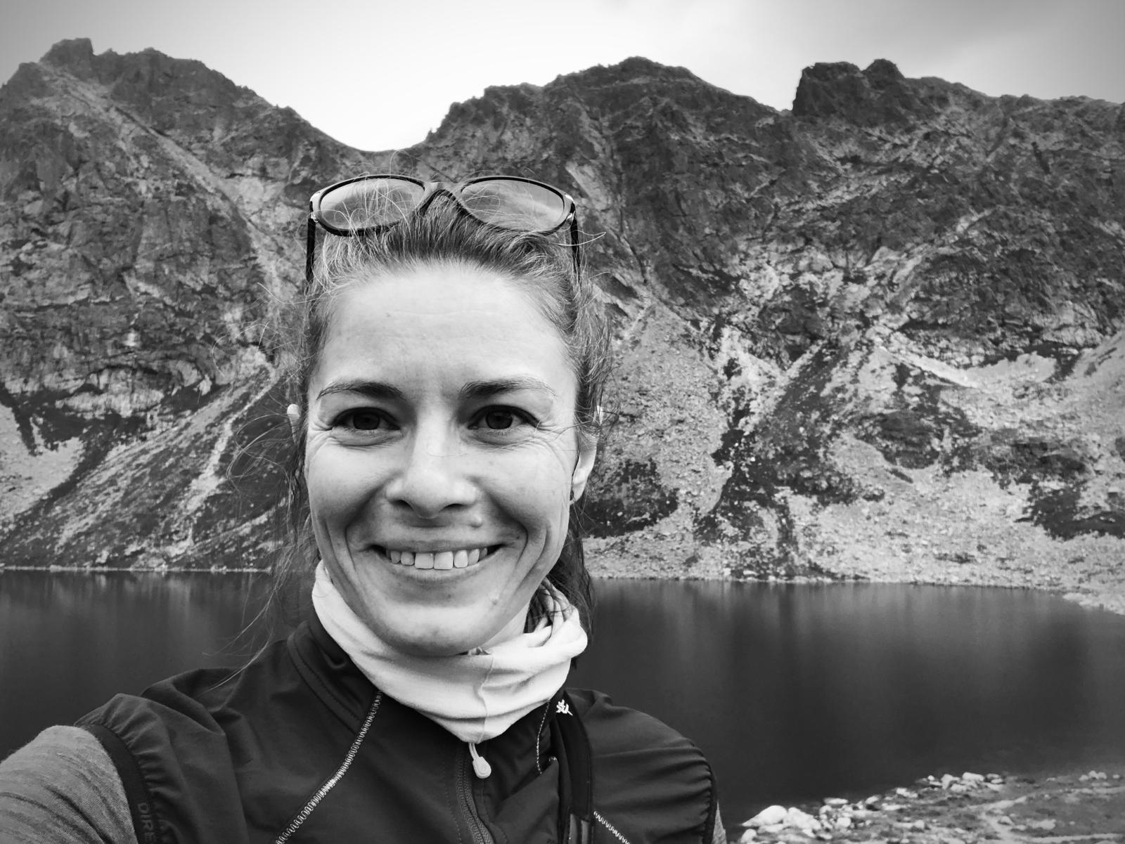 Black and white photo of a smiling woman with mountains in the background.